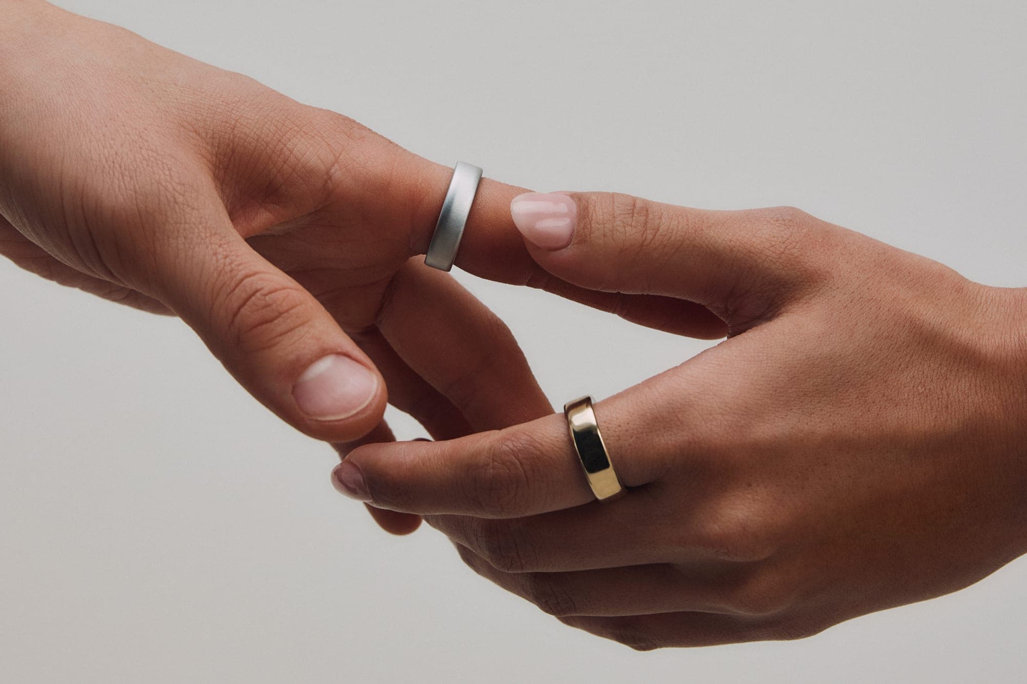 Oura Ring 5 in silver and gold, worn on two hands against a clean neutral backdrop